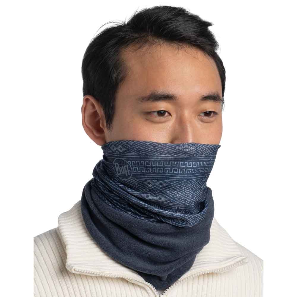 A man wearing a dark blue patterned neck gaiter or balaclava over his lower face and neck, paired with a cream-colored ribbed zip-up sweater, against a plain white background.