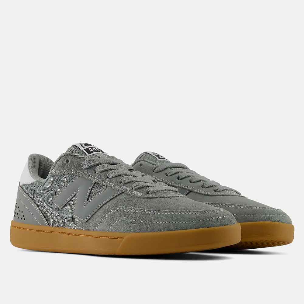 A pair of New Balance low-top sneakers in a muted gray suede and mesh upper with a classic gum rubber sole, shown against a light gray studio background.
