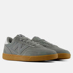 A pair of New Balance low-top sneakers in a muted gray suede and mesh upper with a classic gum rubber sole, shown against a light gray studio background.
