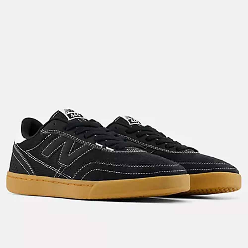A pair of New Balance low-top sneakers in black suede and canvas with white contrast stitching and a gum rubber sole, shown against a light gray background.