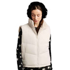 A woman wearing a cream-colored puffer vest over a black long-sleeve top with white star patterns, paired with black earmuffs, against a plain white background.