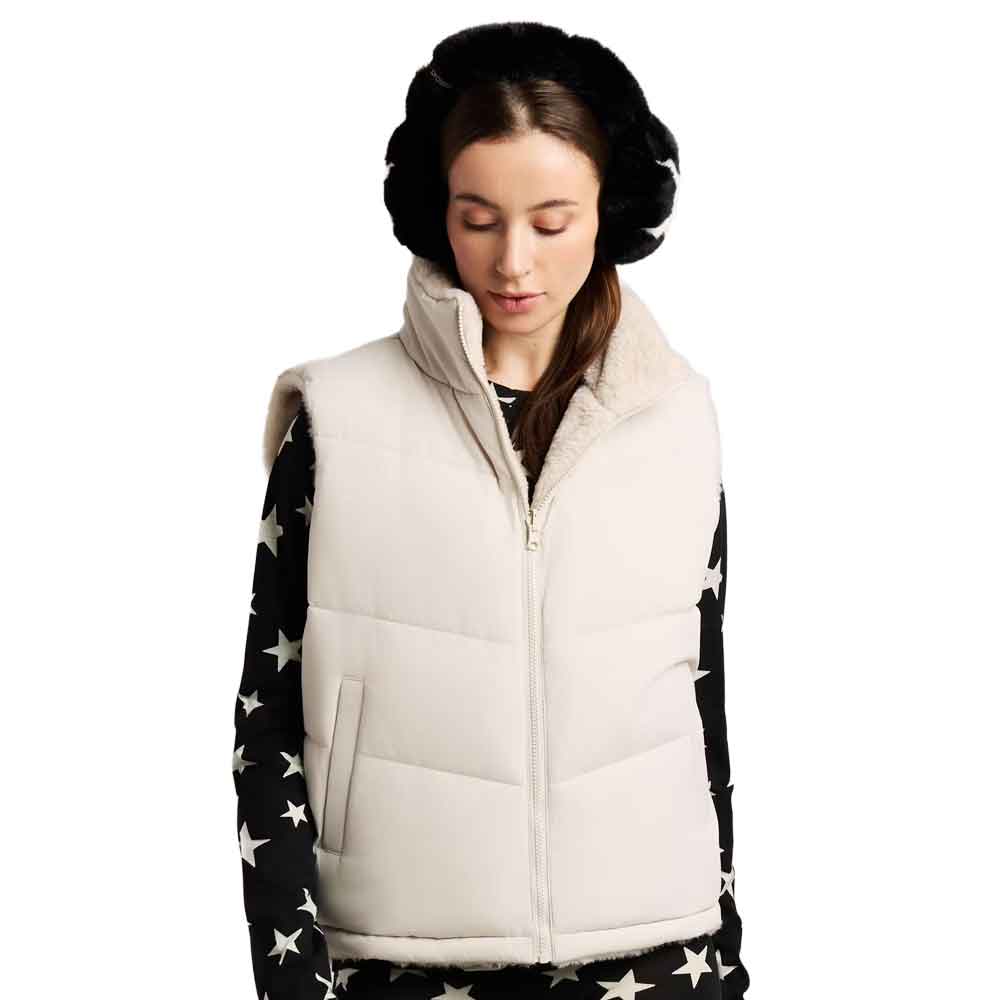 A woman wearing a cream-colored puffer vest over a black long-sleeve top with white star patterns, paired with black earmuffs, against a plain white background.