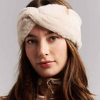 A close-up of a woman wearing a plush, cream-colored twisted headband against a neutral gray background.