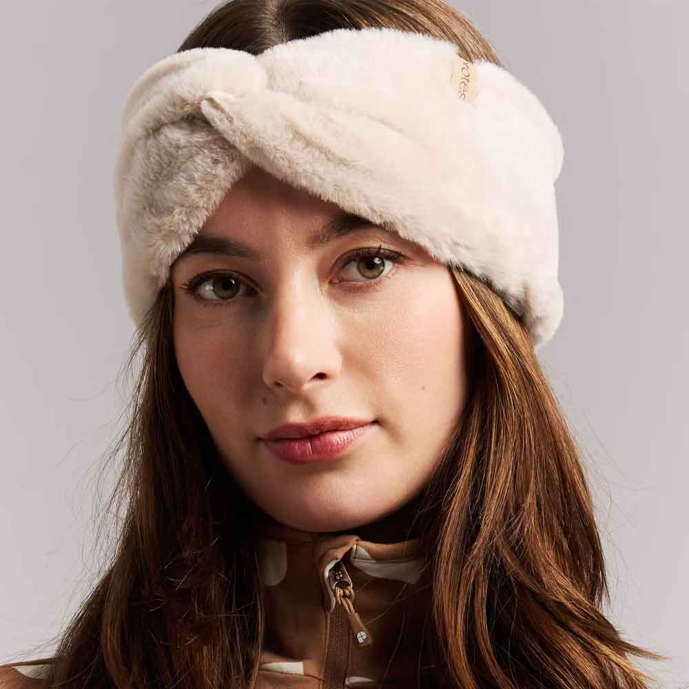A close-up of a woman wearing a plush, cream-colored twisted headband against a neutral gray background.