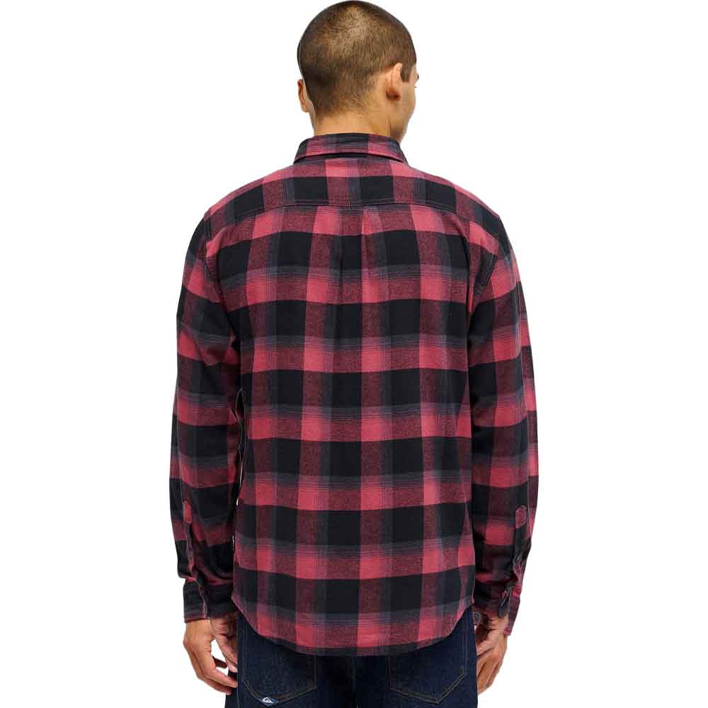 A man viewed from the back wearing a red and black buffalo plaid flannel shirt, paired with dark blue jeans, against a plain white background.