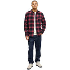 A man modeling a red and black buffalo plaid flannel shirt over a white t-shirt, paired with dark blue jeans and white sneakers, against a plain white background.