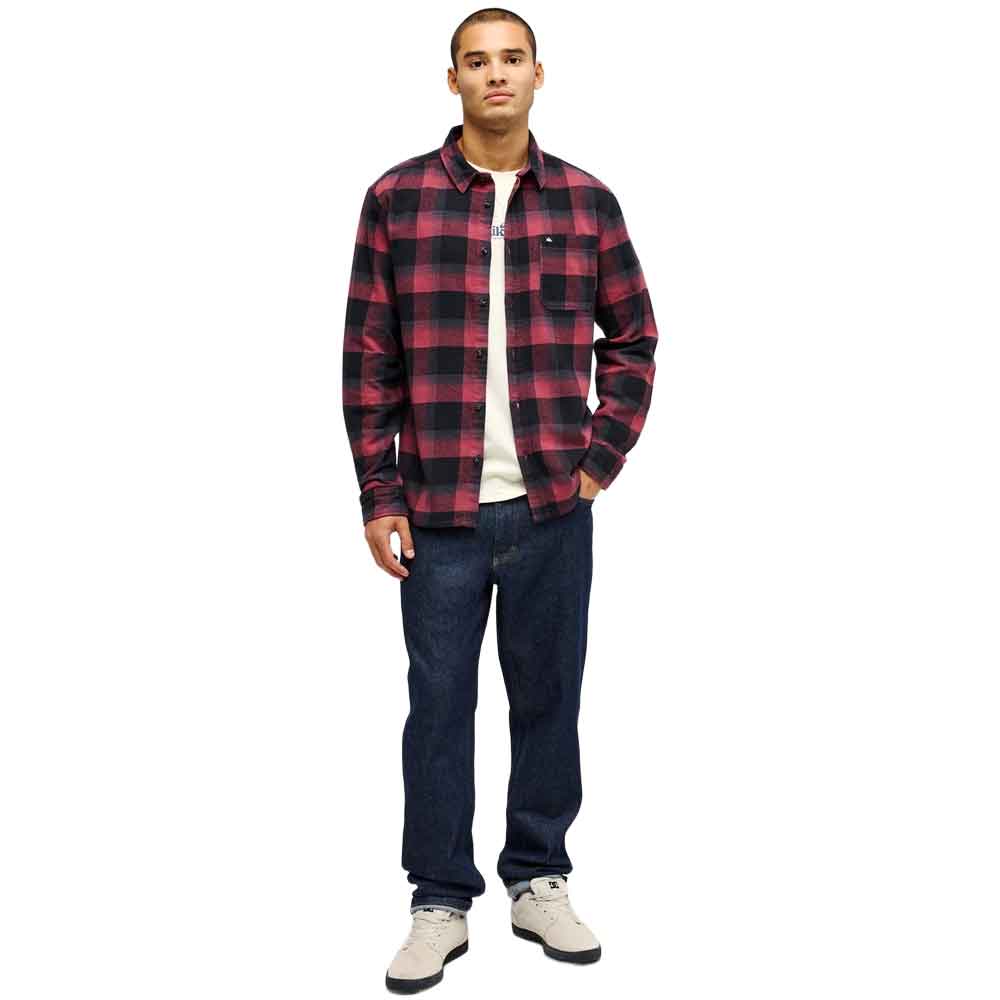 A man modeling a red and black buffalo plaid flannel shirt over a white t-shirt, paired with dark blue jeans and white sneakers, against a plain white background.