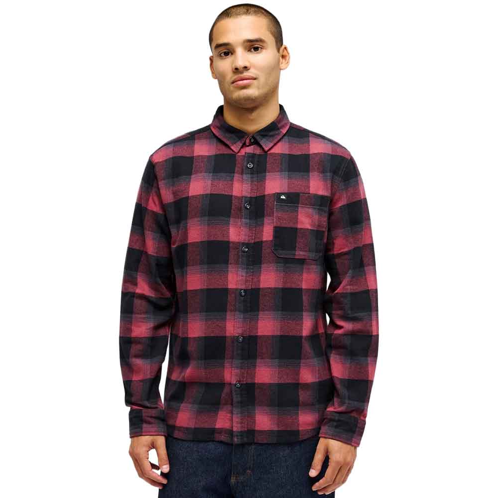 A man wearing a red and black plaid long-sleeve button-up flannel shirt, paired with dark blue jeans, photographed against a solid white background.