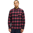 A man wearing a red and black plaid long-sleeve button-up flannel shirt, paired with dark blue jeans, photographed against a solid white background.