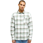 A man wearing a long-sleeve button-up plaid shirt in white, sage green, and brown, paired with blue jeans, against a plain white background.