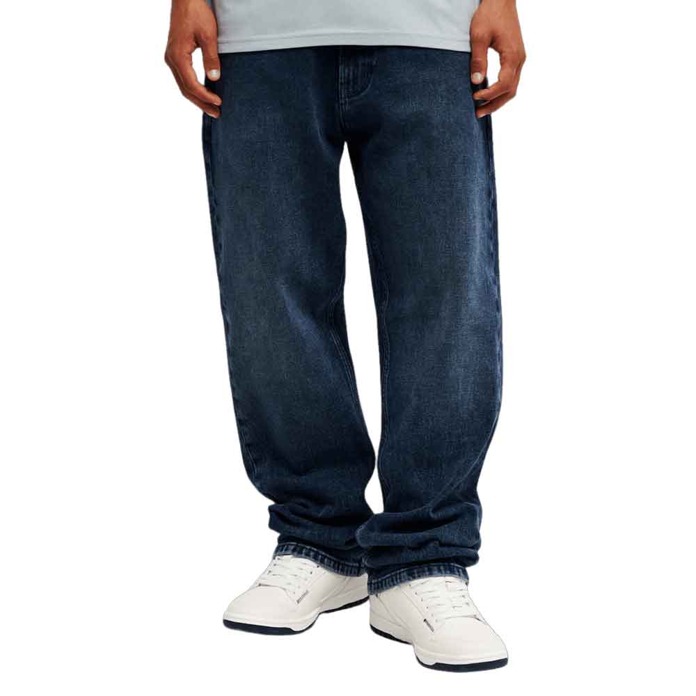 A person wearing dark blue straight-leg jeans with white sneakers, shown from the waist down on a plain white background.