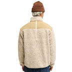 A man viewed from behind wearing a fleece pullover jacket with a tan yoke and a cream sherpa body, paired with a brown beanie and blue jeans against a white background.