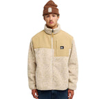 A model wearing a beige and cream fleece zip-up jacket with a tan chest panel, paired with a brown beanie and dark blue jeans, against a plain white background.