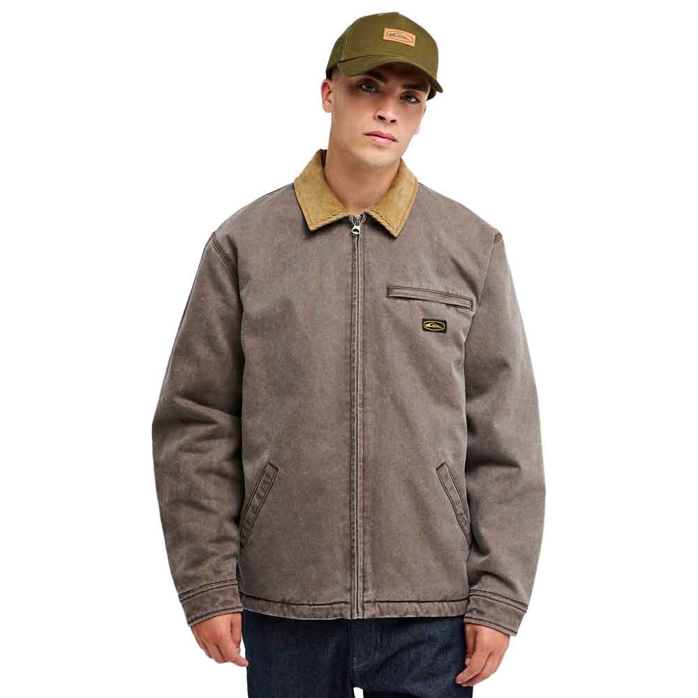 A man wearing a brown quiksilver jacket with a tan corduroy collar, a green cap, and dark blue jeans, photographed against a solid white background.