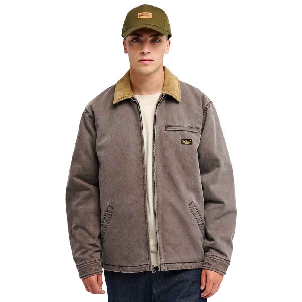 A man wearing a brown work jacket with a tan corduroy collar, an olive green baseball cap, and a cream t-shirt, photographed against a solid white background.