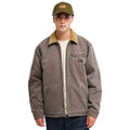 A man wearing a brown work jacket with a tan corduroy collar, an olive green baseball cap, and a cream t-shirt, photographed against a solid white background.