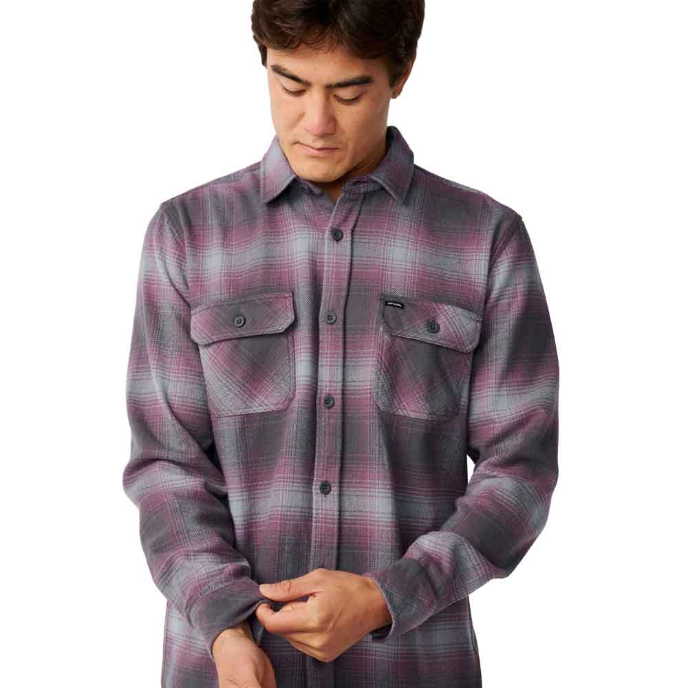 A man wearing a long-sleeve button-up flannel shirt with a gray, purple, and pink plaid pattern, shown against a plain white background.