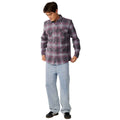 A man wearing a long-sleeve button-up plaid flannel shirt in purple and gray, paired with light blue jeans and black sneakers, standing against a solid white background.