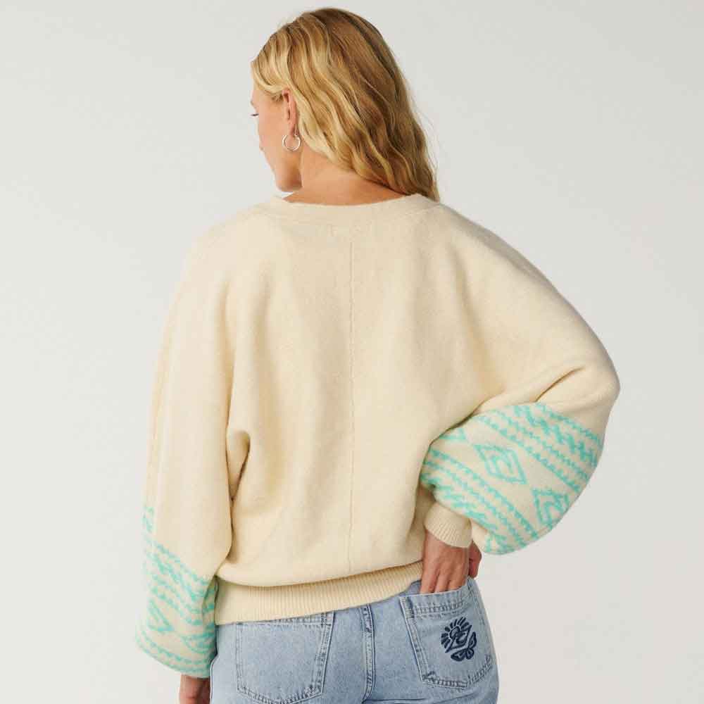 A woman shown from the back wearing a cream-colored knit sweater with mint green geometric patterned cuffs, paired with light blue jeans.