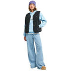 A model wearing a light blue hoodie, a black textured sleeveless vest, wide-leg light blue jeans, a purple beanie, and tan slip-on shoes, standing against a plain white background.