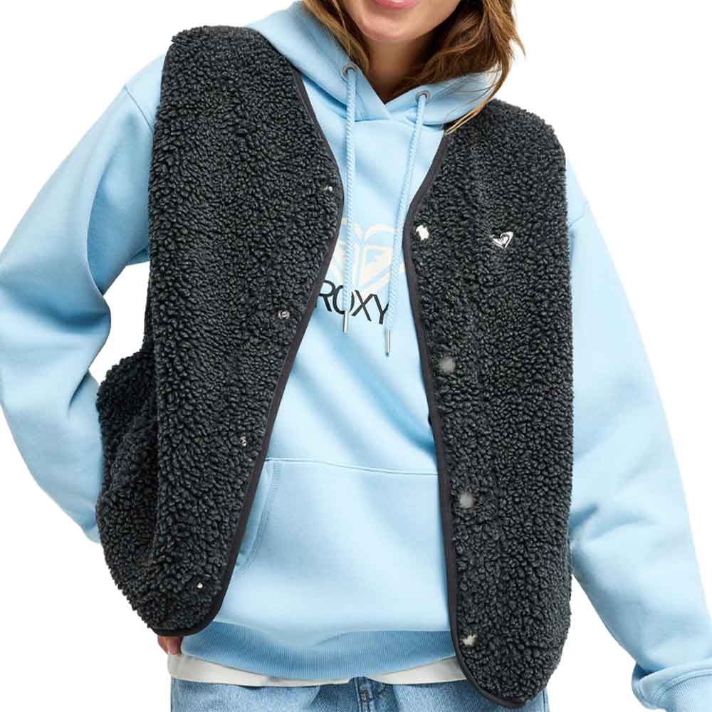 A person wearing a light blue hoodie with a black sherpa fleece vest layered over it, shown from the neck down against a plain white background.