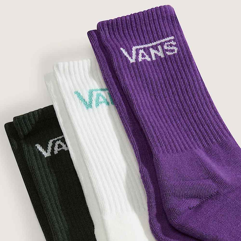 Three pairs of ribbed crew socks in black, white, and purple, arranged diagonally. Each sock features the Vans logo embroidered near the cuff in white, mint green, and purple respectively, against a light beige background.