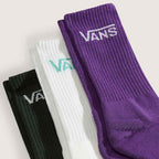 Three pairs of ribbed crew socks in black, white, and purple, arranged diagonally. Each sock features the Vans logo embroidered near the cuff in white, mint green, and purple respectively, against a light beige background.