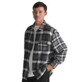 A man wearing a black and gray plaid flannel overshirt over a white t-shirt, photographed against a solid white background.