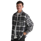 A man wearing a black and gray plaid flannel overshirt over a white t-shirt, photographed against a solid white background.