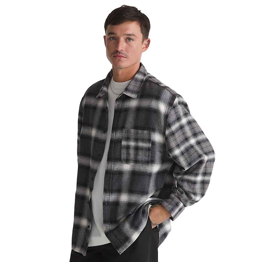 A man wearing a black and gray plaid flannel overshirt over a white t-shirt, photographed against a solid white background.