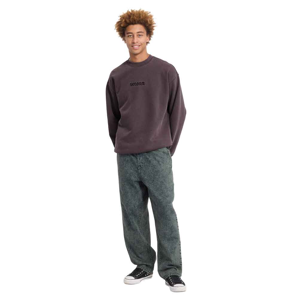 A model wearing a dark brown crewneck sweatshirt with a small black 'uniqlo' logo on the chest, paired with dark gray relaxed-fit jeans and black sneakers, standing against a solid white background.