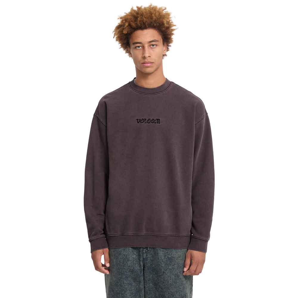 A model with curly light brown hair wearing a dark brown washed crewneck sweatshirt with 'WOOOO' embroidered on the chest, paired with gray jeans, against a plain white background.