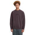 A model with curly light brown hair wearing a dark brown washed crewneck sweatshirt with 'WOOOO' embroidered on the chest, paired with gray jeans, against a plain white background.