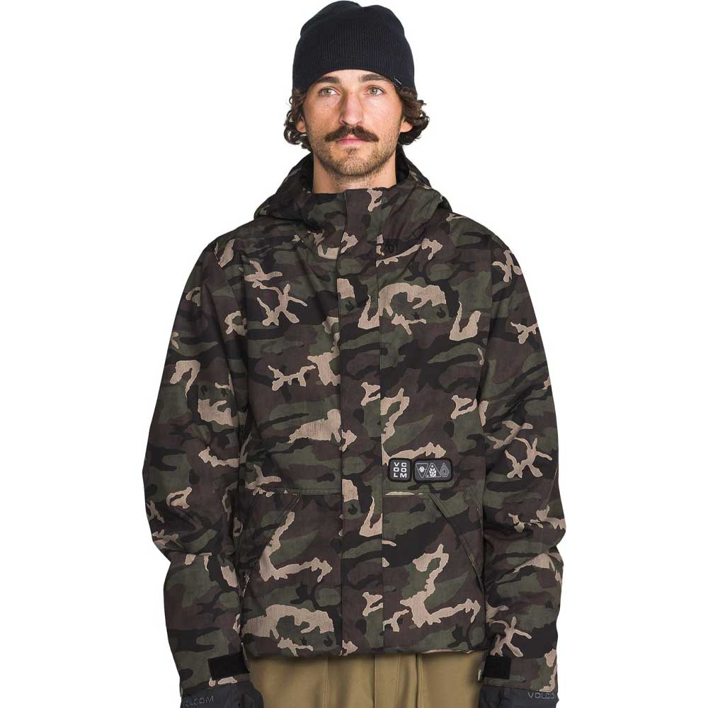 A man wearing a camouflage-patterned hooded jacket, a black beanie, and olive pants, photographed against a solid white background.
