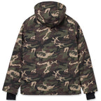 A hooded camouflage jacket shown from the back, featuring an all-over woodland camo pattern in green, brown, black, and beige, with black cuffs.