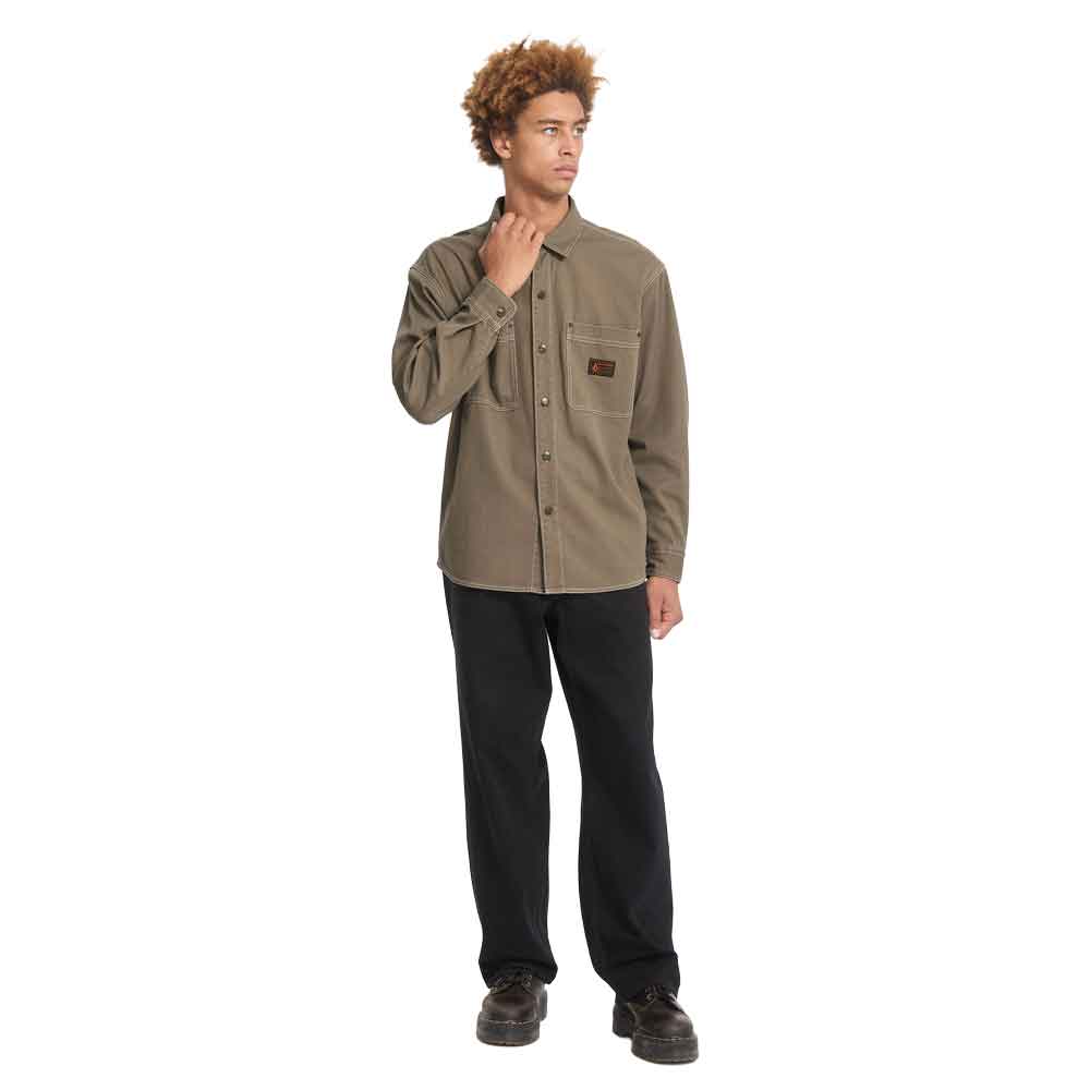 A man modeling a muted olive-brown long-sleeve button-up shirt with a chest pocket, paired with black pants and dark shoes, against a plain white background.