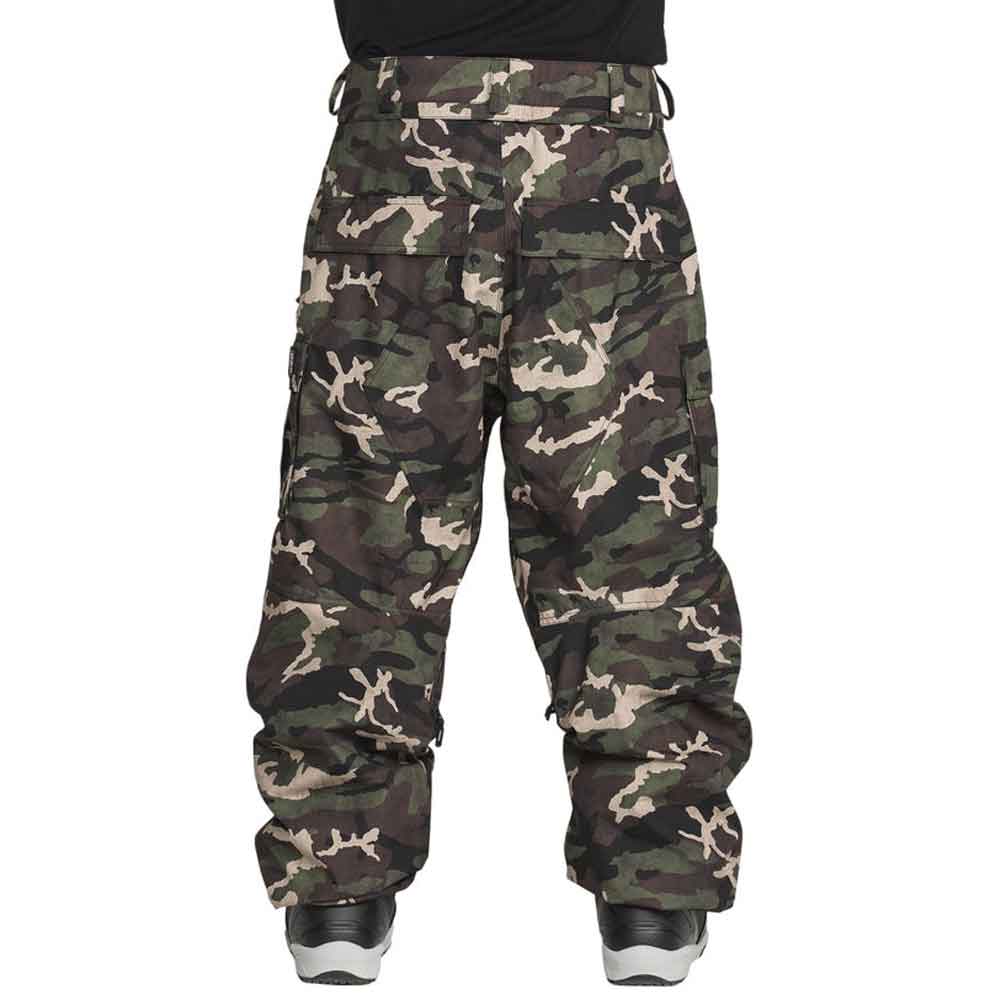 A pair of camouflage cargo snow pants shown from the back, featuring a green, brown, and beige woodland camo pattern, worn by a model with a black shirt and sneakers visible at the bottom.