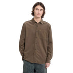 A man wearing a brown corduroy button-down shirt with a chest pocket, paired with gray jeans, photographed against a solid white background.